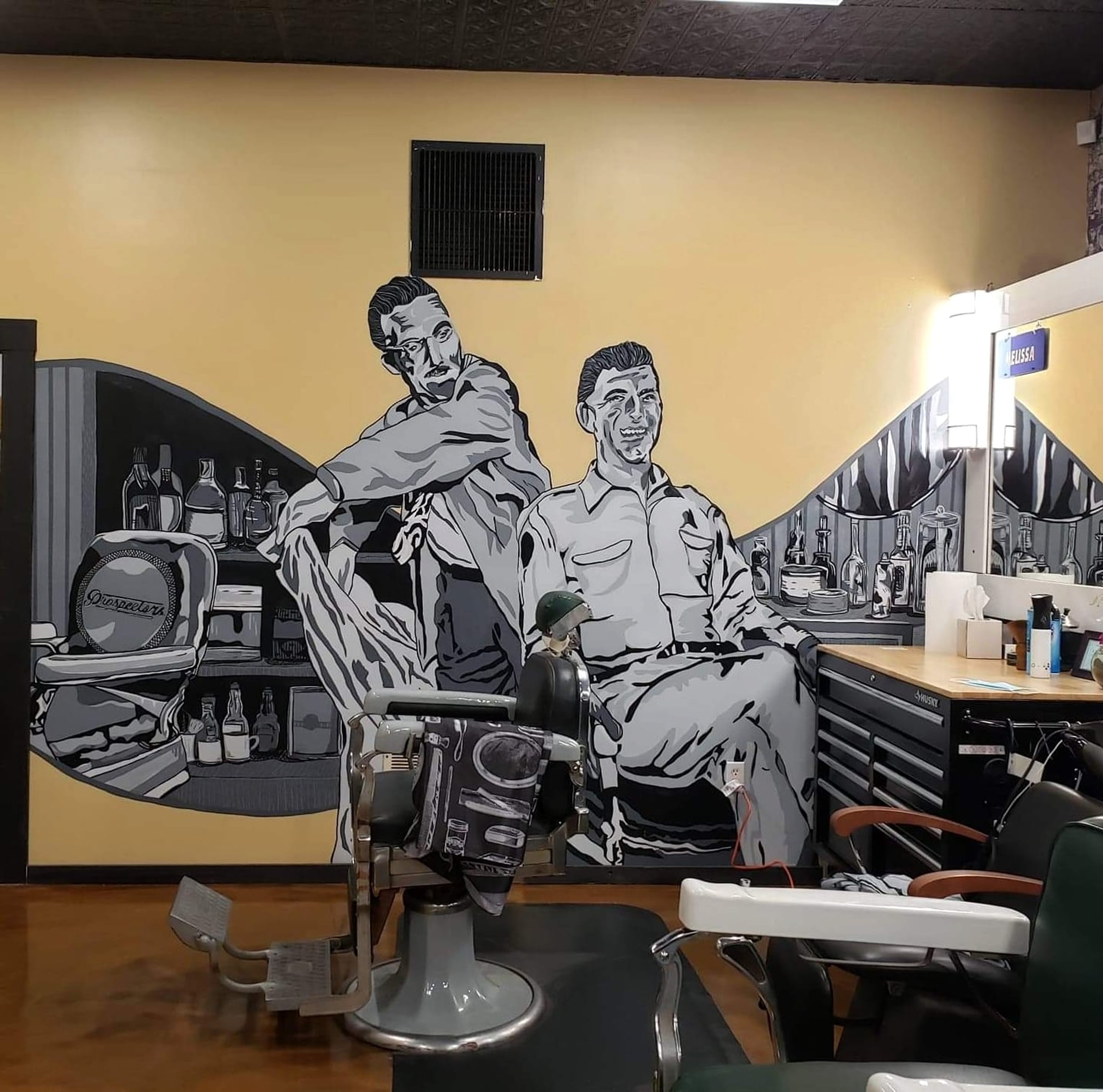 A vintage barbering mural and barber chairs inside the shop
