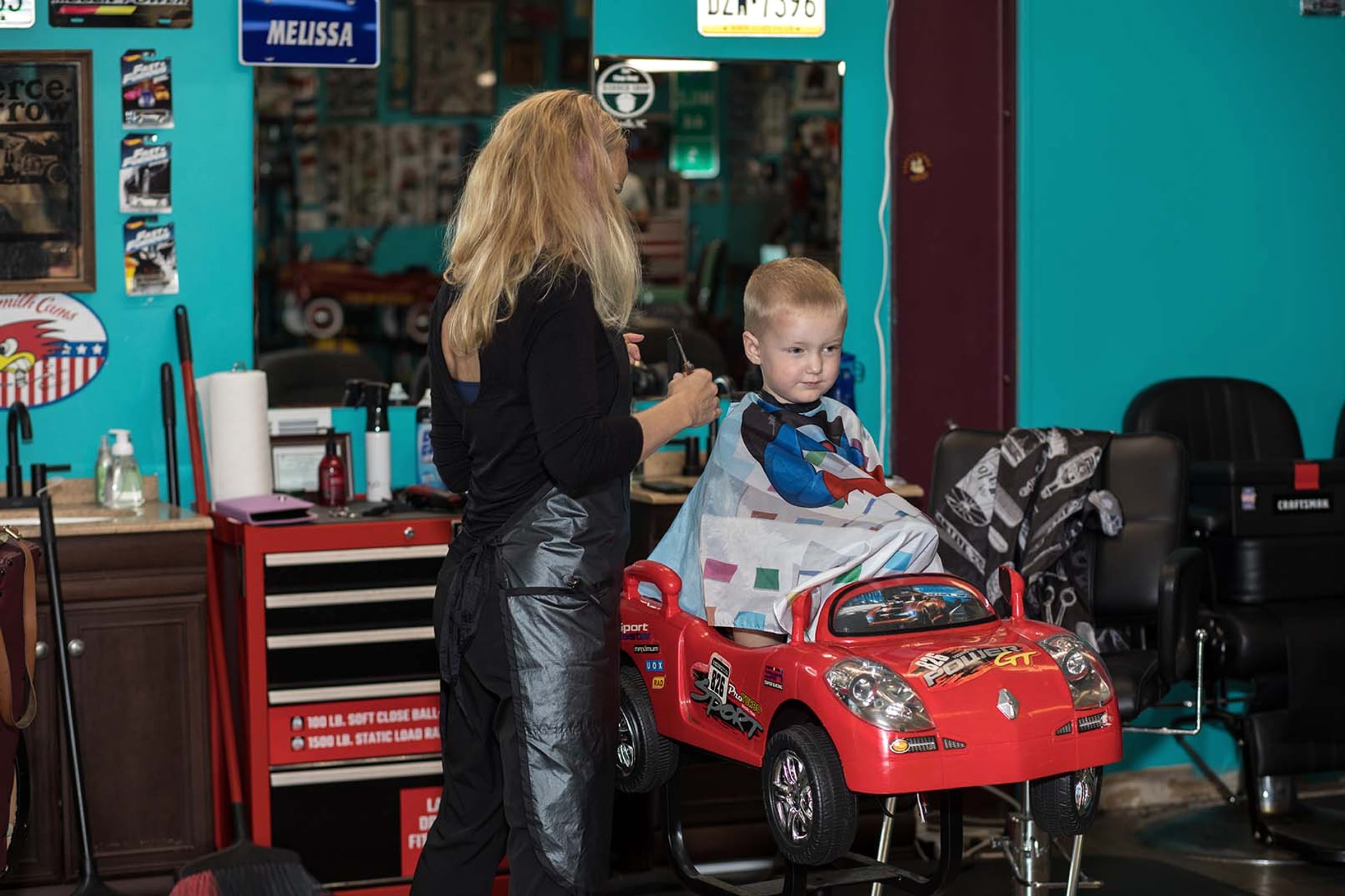 A barber giving a young child a haircut in a red car chair